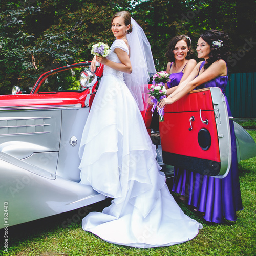 Bride stands on a doorstep of an old vintage car while bridesmai photo