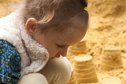 Little girl playing on the beach . The small child at a playground . Sitting in sandboxes  photo