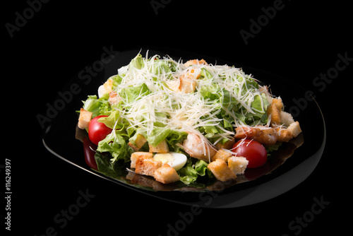 Caesar salad with prawns, cherry tomato and cheese on black plate