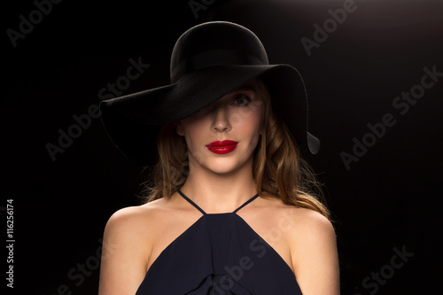 beautiful woman in black hat over dark background