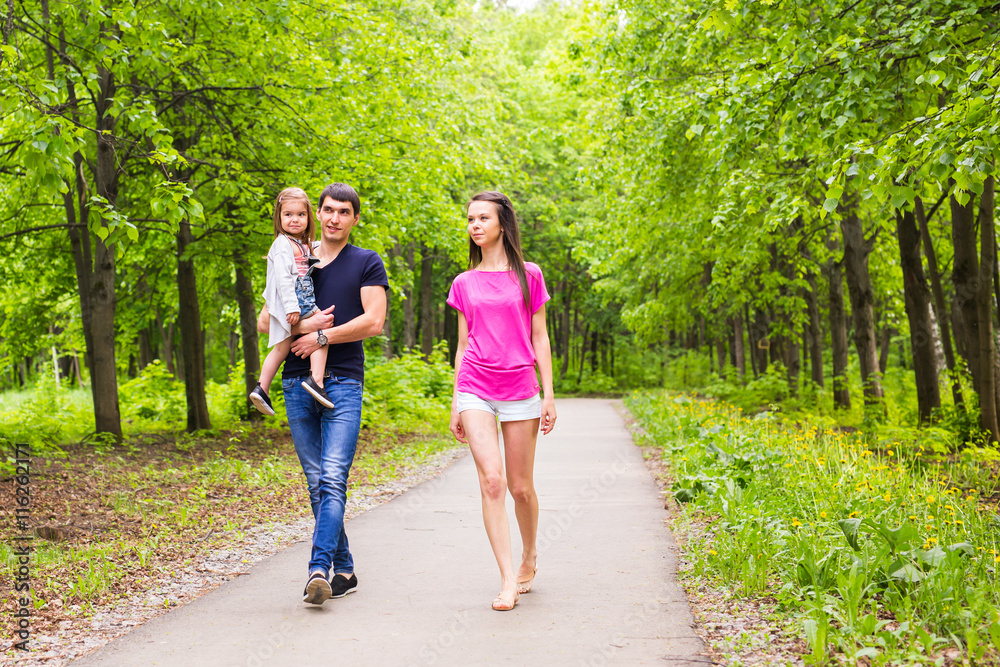 Happy young family walking down the road outside in green nature