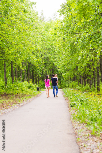 Happy young family walking down the road outside in green nature