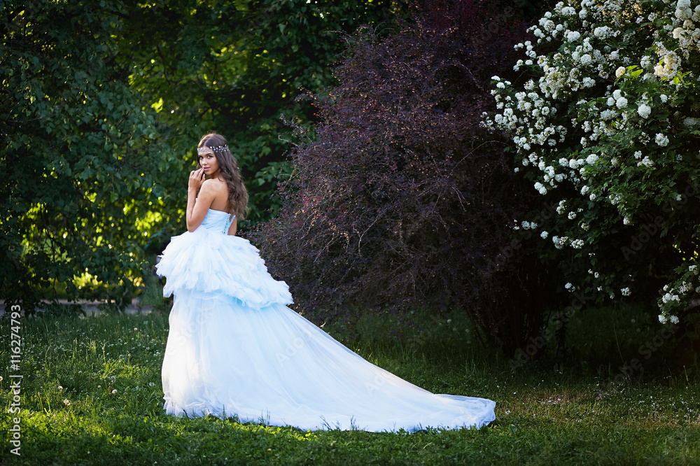 Gorgeous brunette in a lush blue dress with her hair is set in a lush garden