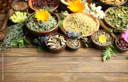 Herb selection and fresh flowers in bowls on wooden background