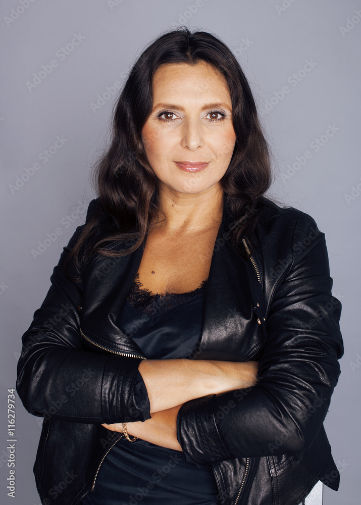 pretty brunette confident stylish real mature woman sitting on chair in  studio, sexy on gray background wearing leather jacket Stock Photo | Adobe  Stock
