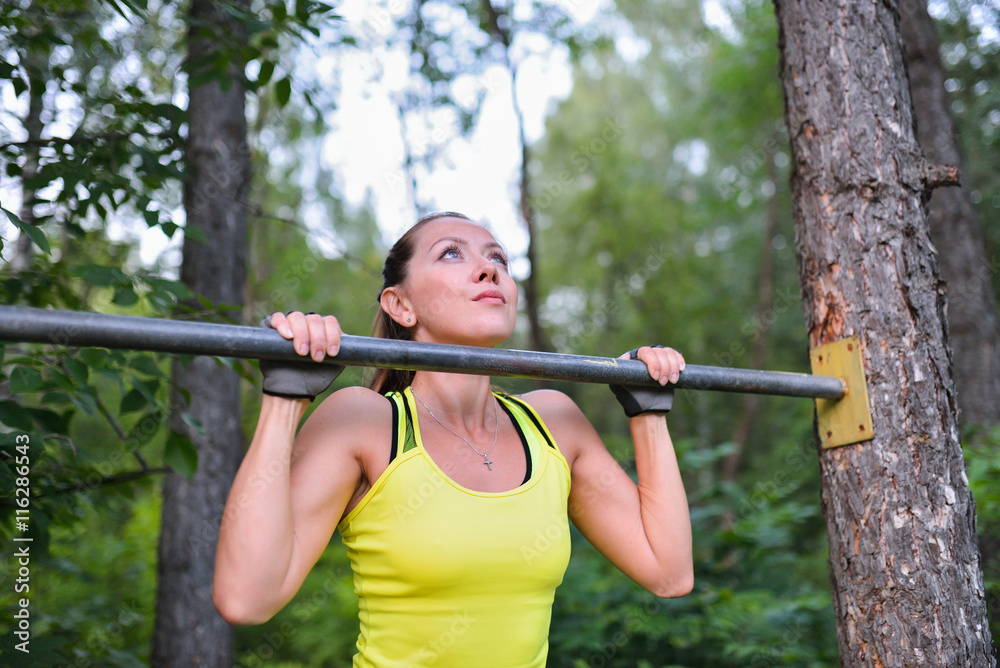 Fit woman training pull ups on horizontal bar in city park outdoors