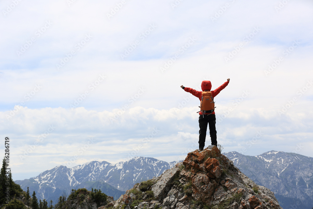 Obraz premium cheering successful woman backpacker open arms on mountain peak