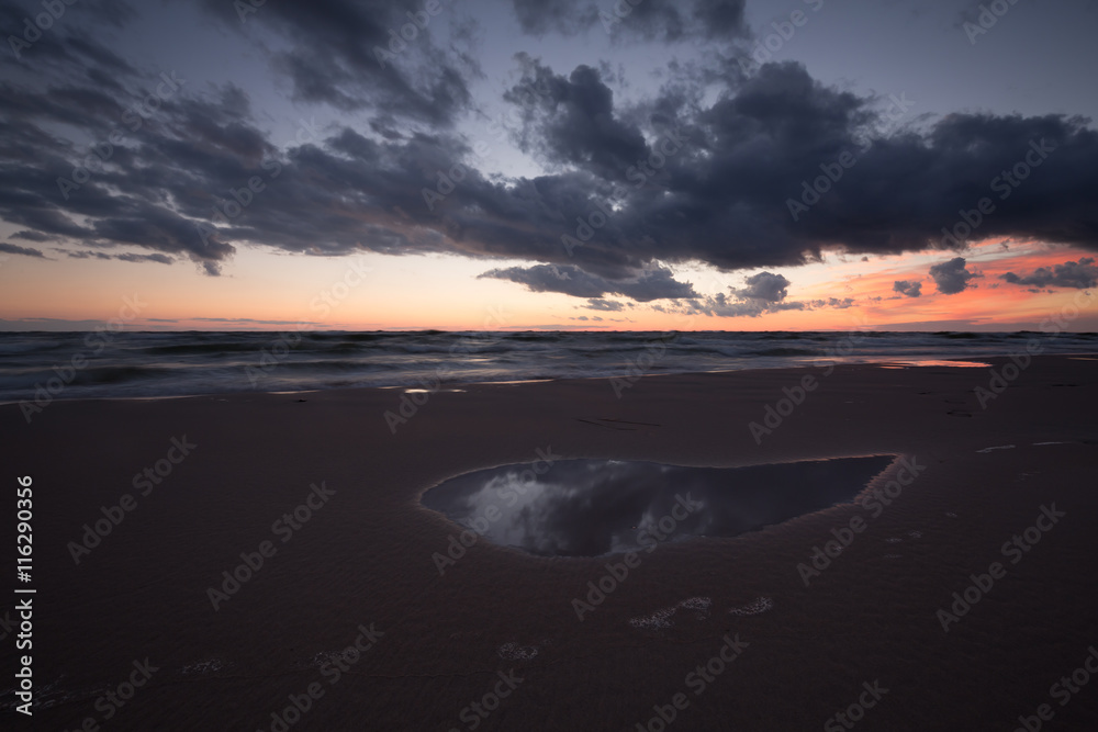 Sunset at the beach with the clouds reflecting in a pool of water