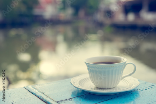 Cup of hot coffee on old wooden table and view of sunrise in the river background.Vintage tone with copy space. © Travel man