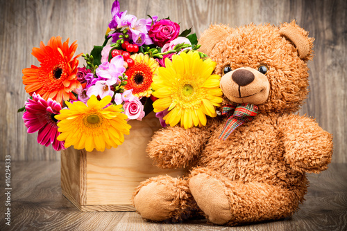 Beautiful flowers and a teddy bear on wooden background