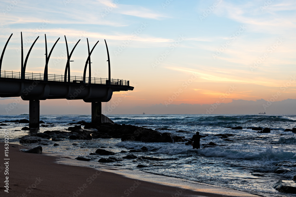 Man performing religious ritual next to the Millennium Pier in Umhlanga Rocks at Sunrise, with ships on the Indian Ocean in the background
