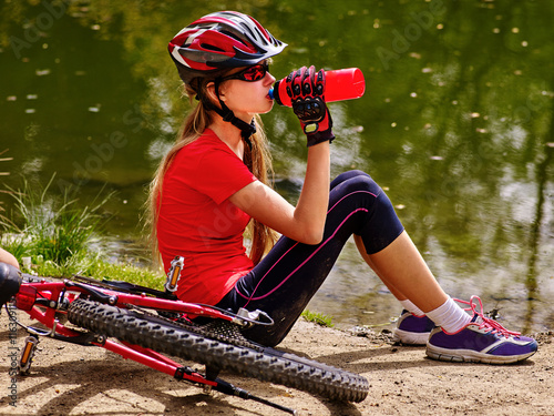 Bicycling girl. Girl wearing bicycling helmet rides bicycle. Girl bicycling drinking of bottle water. Bicycling is good for health concept.