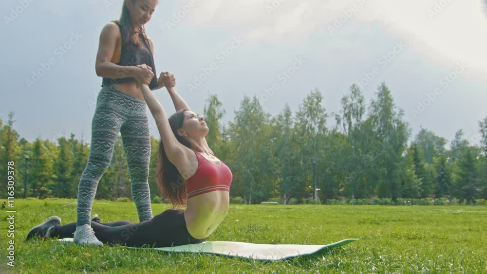 Young sport women doing stretching exercises for the spine in the park, dolly shot