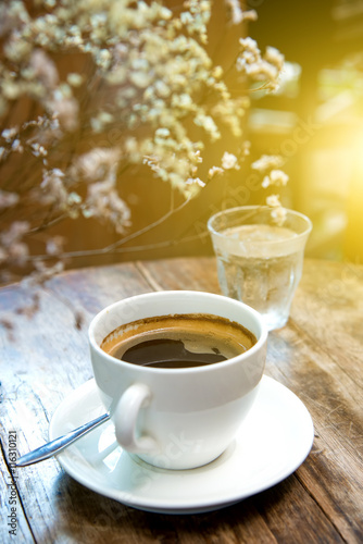 White coffee cup with dry flower on wooden table.