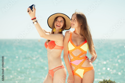 two smiling young women on beach making selfie