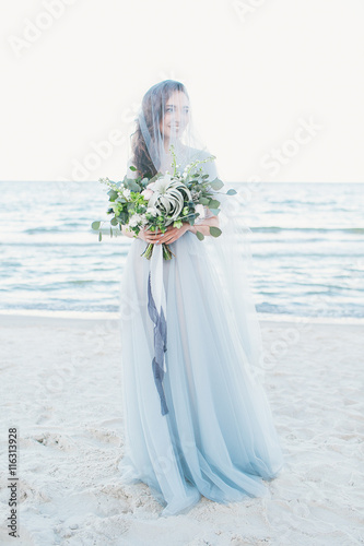 Tender bride in veil with wedding bouquet  by the sea