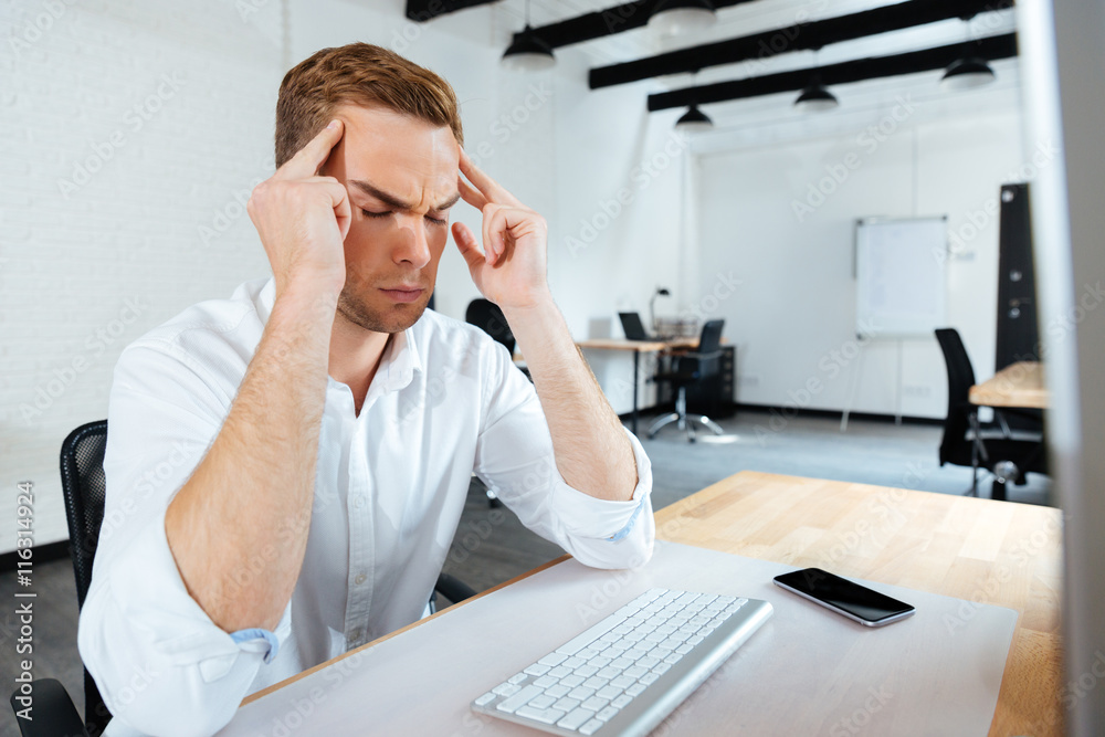 Stressed young businessman having a headache in office Stressed young businessman having a headache in office