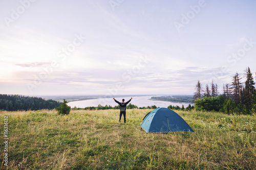 Hiker meets good morning with raised hands just got out from his tent