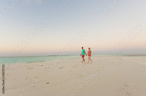 Honeymoon couple holding hands walking on perfect white sand beach. Newlyweds happy in love relaxing on summer holidays in sunny tropical paradise destination. Travel vacation concept.