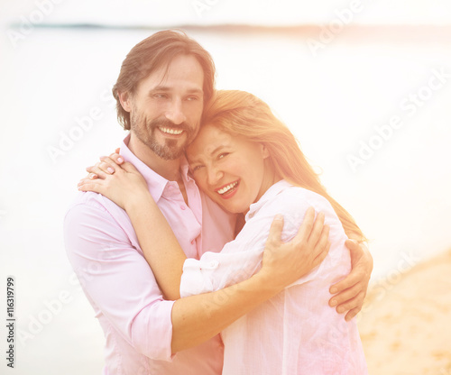 Romantic concept. Toned picture of smiling attractive middle-aged couple relaxing at beach and posing together for portrait in hot summer sun.