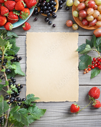 Sheet paper with fresh berries and branches with currant on wooden background. Copy space, top view, high resolution product.