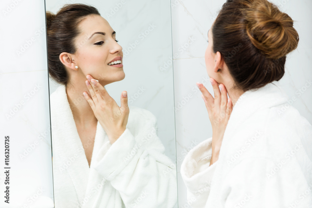 Young woman caring of her skin standing near mirror in the bathr Young woman caring of her skin standing near mirror in the bathr