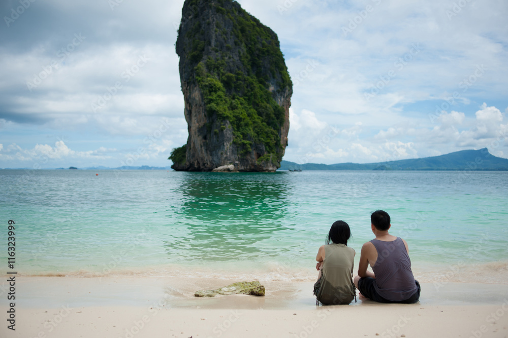 Back view of young couple sitting by the sea.
