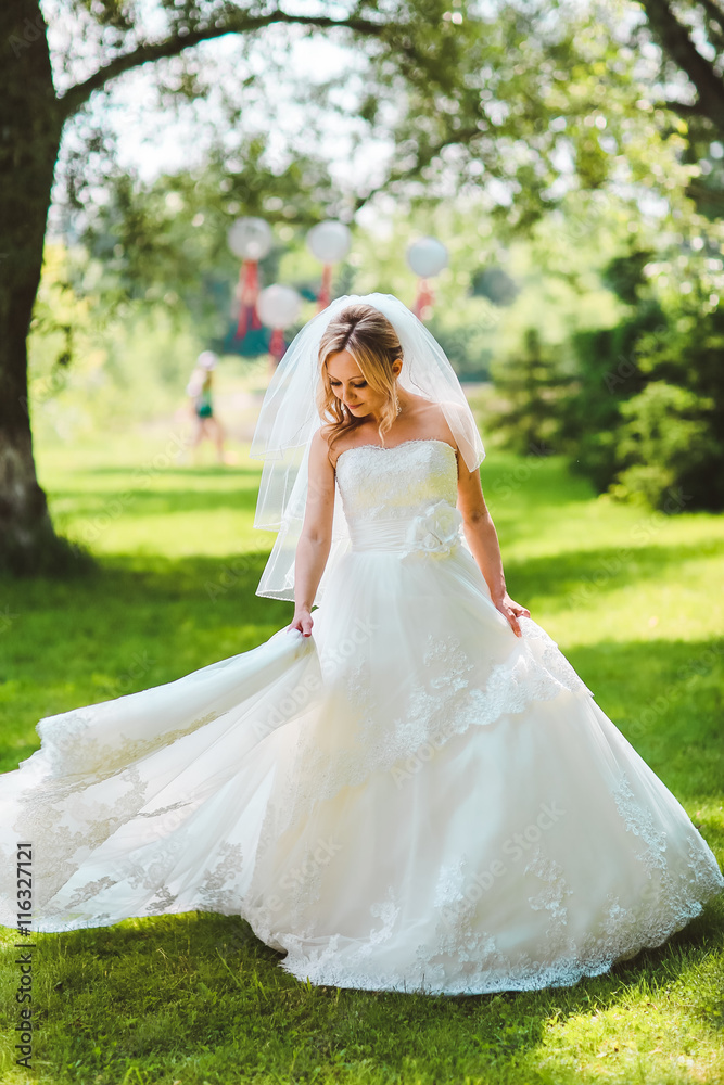 Beautiful romantic stylish blonde bride in white dress dancing in the forest in the sun. Summer meadow park. Woman turn around in white dress.