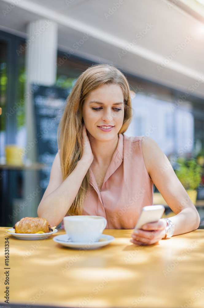 Portrait of smiling woman sitting in a sidewalk cafe looking at her smartphone Portrait of smiling woman sitting in a sidewalk cafe looking at her smartphone