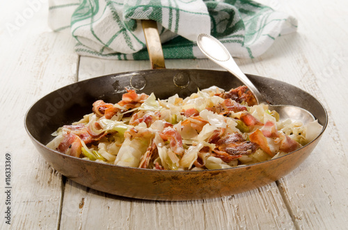 fried white cabbage and bacon in a brass pan