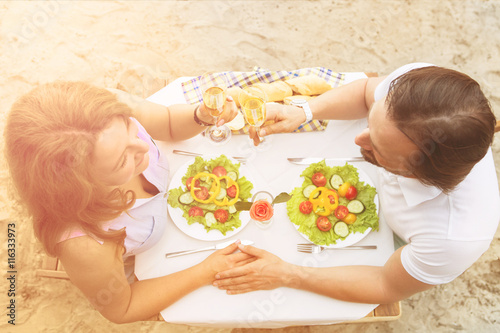 Handsome man and beautiful woman holding hands and resting in restaurant or cafe. Closeup toned top view picture of table with delicious lunch or dinner.