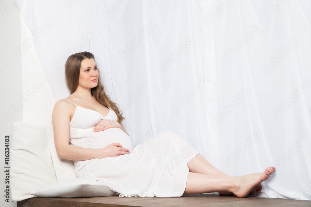beautiful pregnant woman in white dress near window beautiful pregnant woman in white dress near window