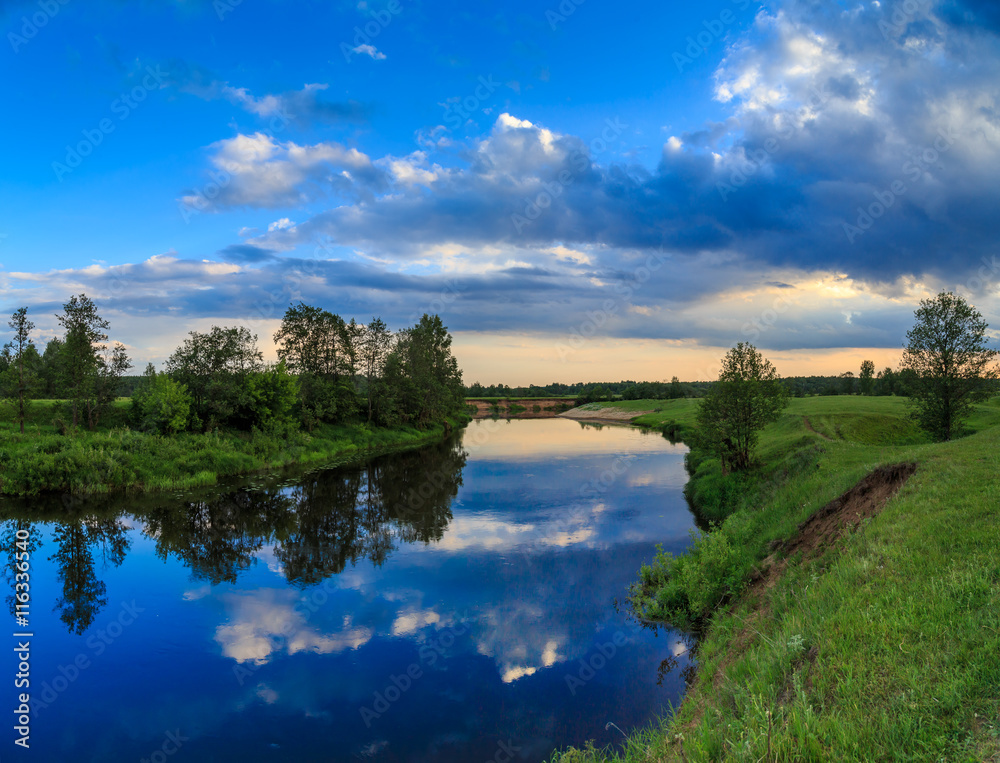 Sky with light clouds reflected in the river, field, trees, summer evening