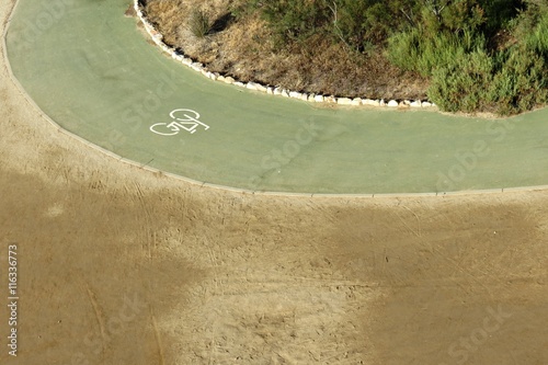 Carril bici en curva junto a vegetación mediterránea y arena photo