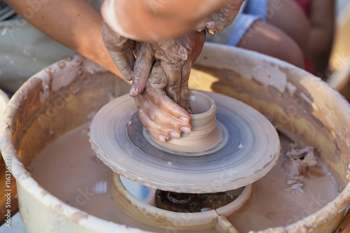 Hands of potter, creating an earthen jar on the circle, close-up