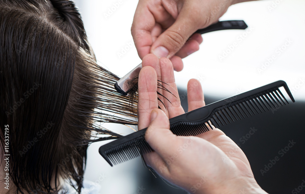 Obraz premium Ścinanie włosów brzytwą, dłonie fryzjera ścinającego włosy