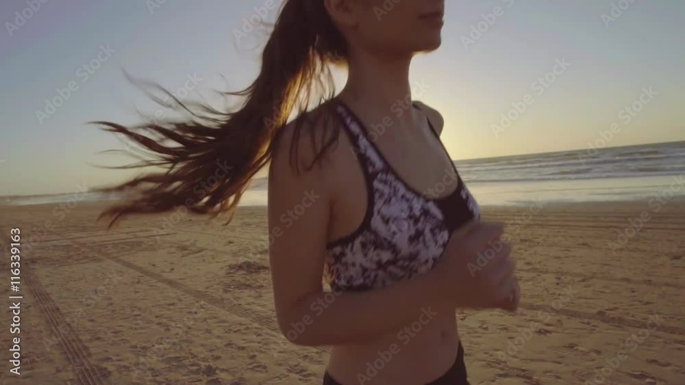 Chica joven corriendo en camara lenta al atardecer en la playa