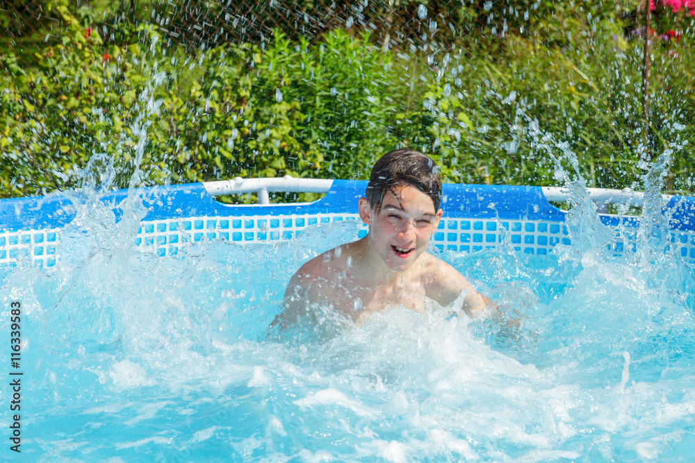Cute teen boy enjoying summer splashing water in a swimming pool