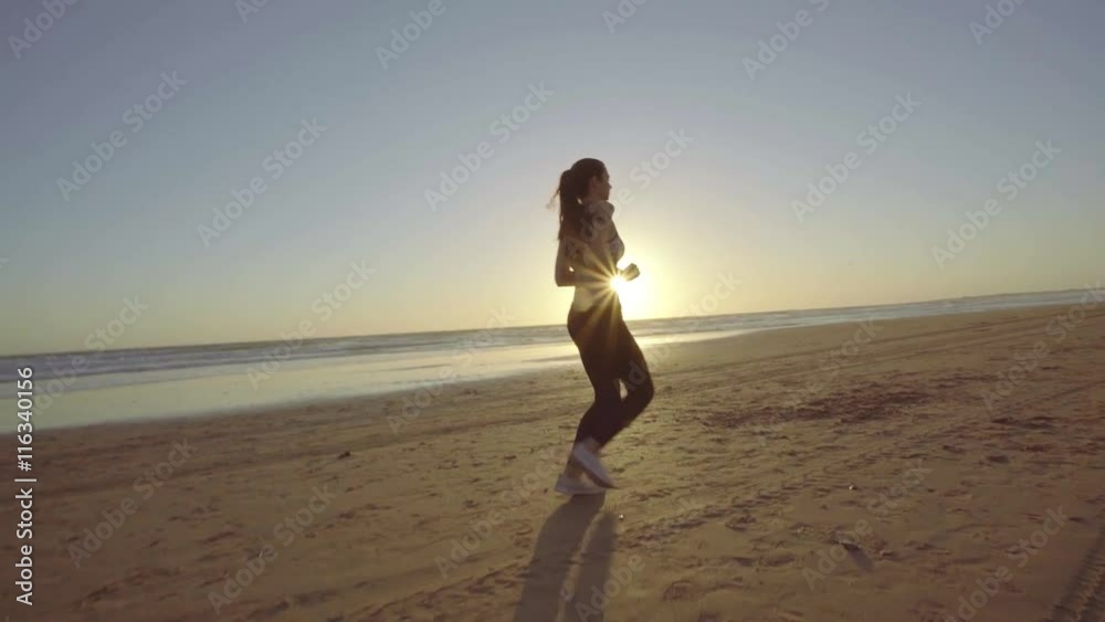 Chica joven corriendo en camara lenta al atardecer en la playa