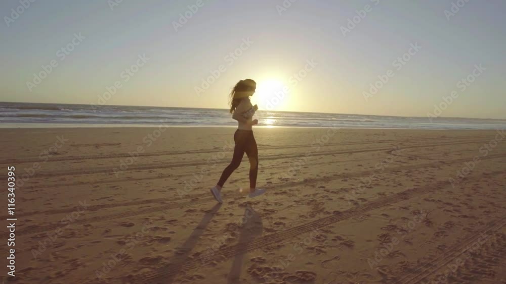 Chica joven corriendo en camara lenta al atardecer en la playa