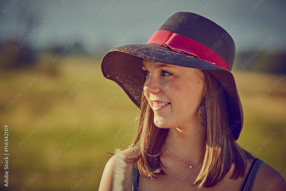 Giovane ragazza con cappello, serena al sole in campagna