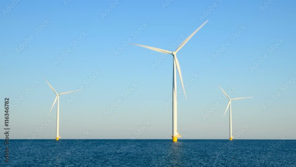 Wind turbines with rotating blades in an offshore wind park during a beautiful summer day.