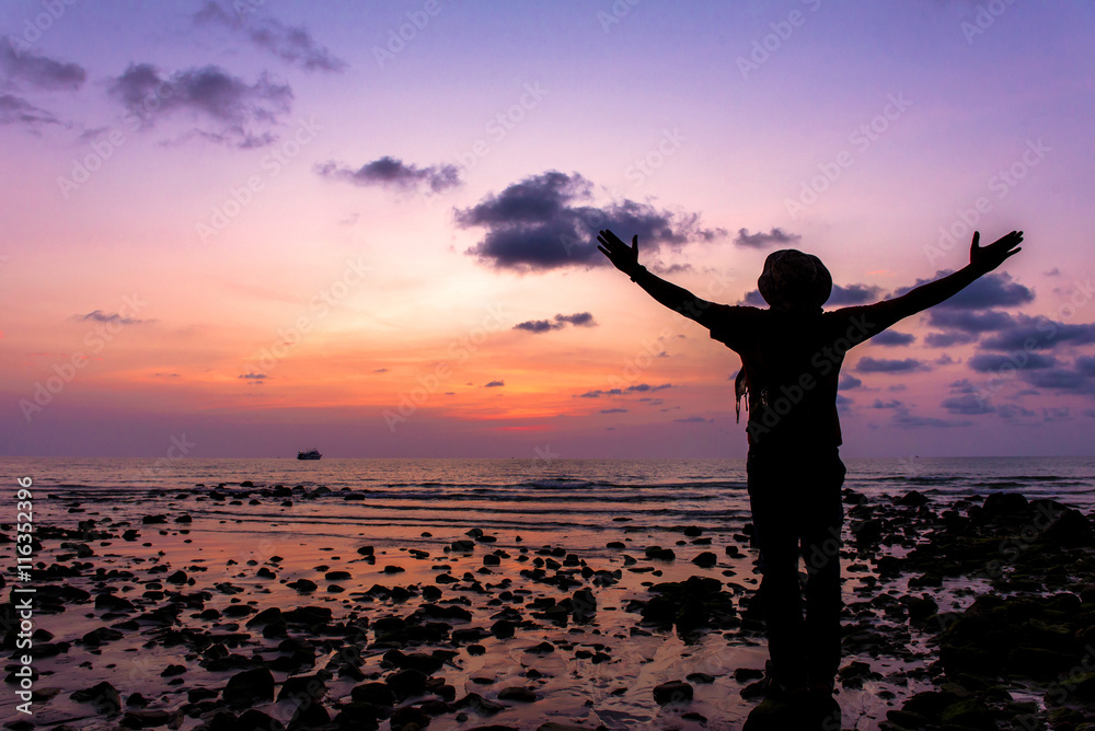 Silhouette of traveler with hands up in the sunset on the ocean Silhouette of traveler with hands up in the sunset on the ocean