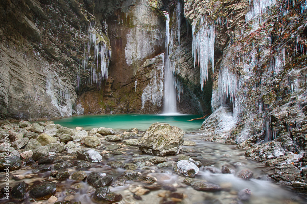 Fototapeta premium Frozen waterfall Kozjak in Slovenia with icicles and green water river pool .