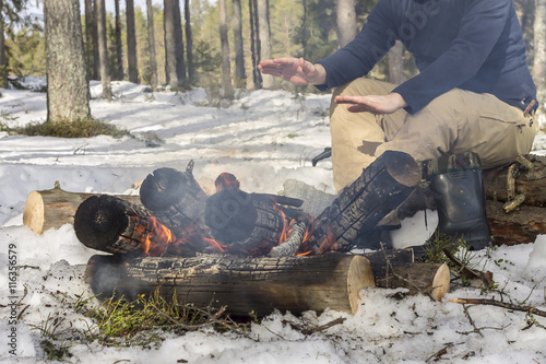 man warming his hands around a campfire in the forest