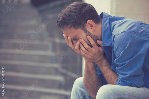 Foto Traurige junge betonte Mann draußen mit den Händen hält Kopf sitzt weinend