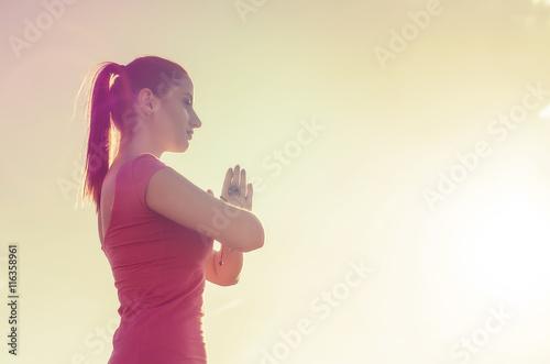 woman practicing yoga meditating in the open field on a sunset sky background