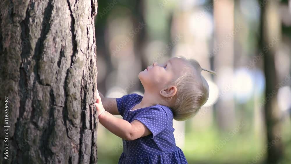 Baby girl one year old playing hide and seek with her mom, hiding behind a big tree, close-up Baby girl one year old playing hide and seek with her mom, hiding behind a big tree, close-up