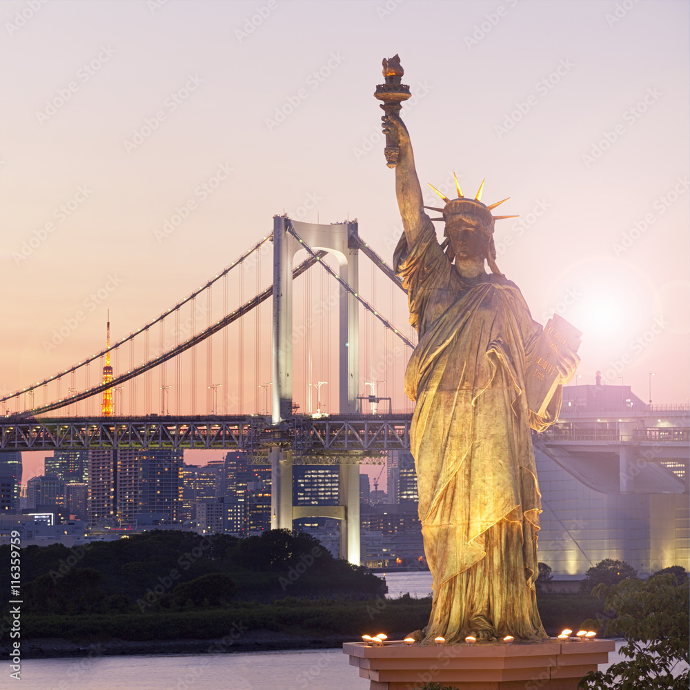 Fototapeta premium Statue of Liberty and Rainbow bridge, located at Odaiba Tokyo, with Tokyo skyline in background at twilight