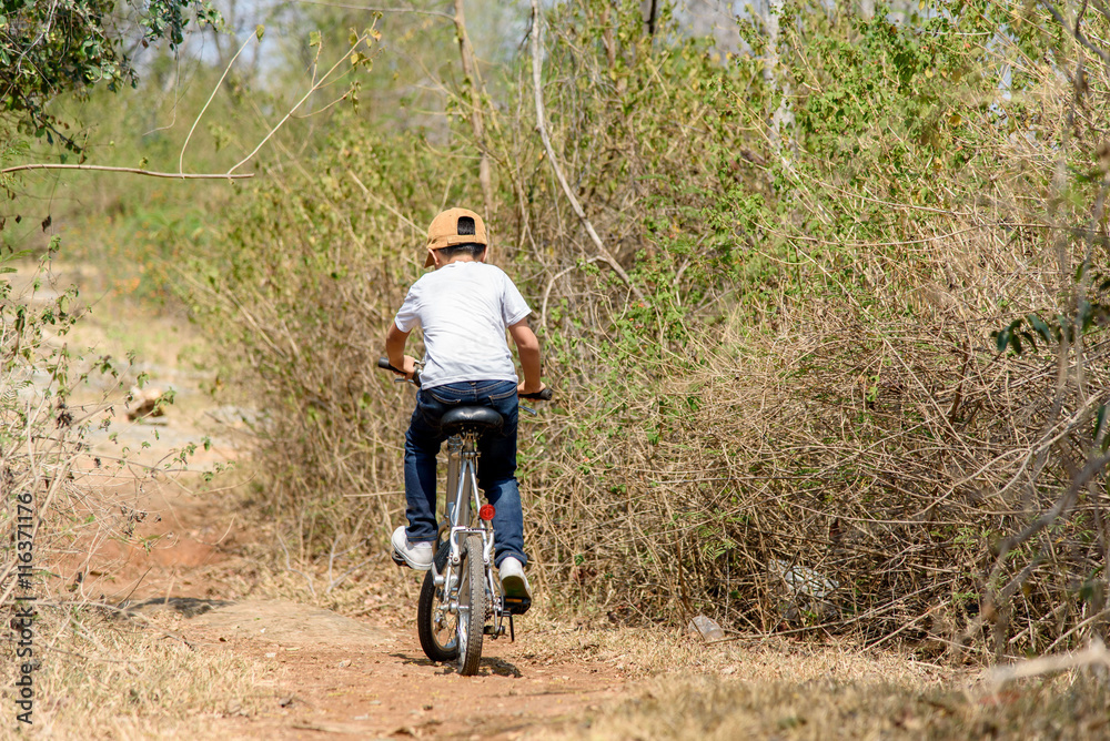 Naklejka premium Little boy ride bicycle on the rock road.